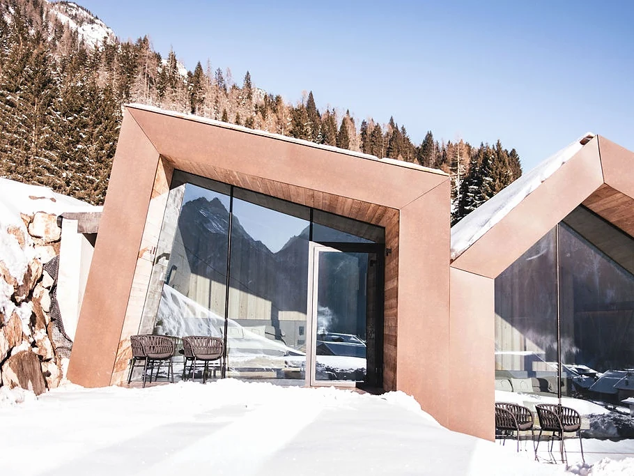 Esterno del Mountain Lodge con ampie vetrate riflettenti tra la neve e il bosco di conifere