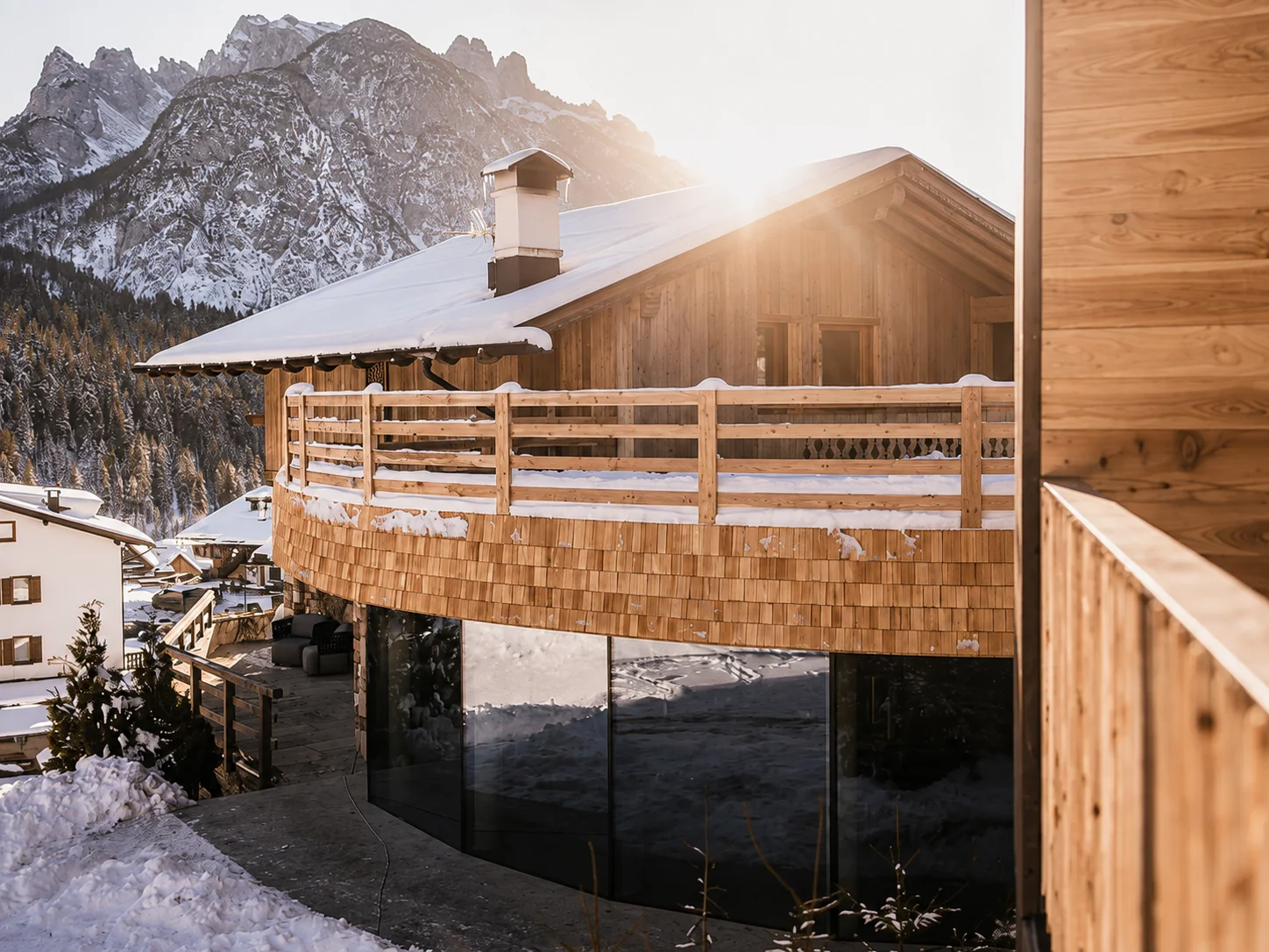 Lo chalet in legno illuminato dal sole con le cime dolomitiche sullo sfondo